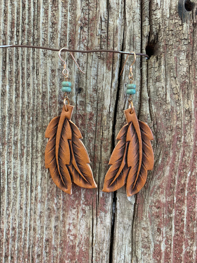 Double Hand-tooled Leather Feather Earrings with Turquoise in Natural hanging from a wire.