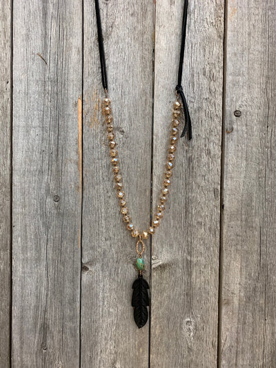 J.Forks Designs necklace on wooden backdrop. This is a 30" Golden Austrian Crystal, bronze and black leather back necklace with turquoise, hand tooled leather feather. 