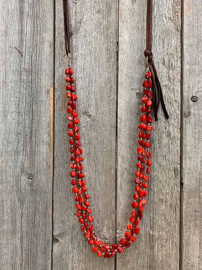 J.Forks Designs necklace hanging on wooden backdrop. This is a three-strand 32" red coral with turquoise seed beads and chocolate leather back necklace.