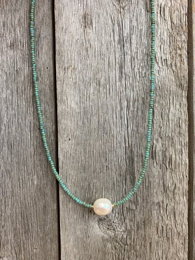 J.Forks Designs necklace hanging on wooden backdrop. This is 16" turquoise seed bead necklace with a freshwater pearl center.