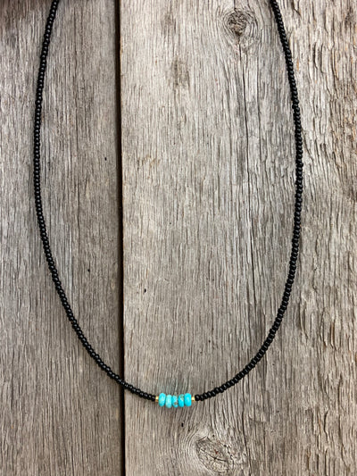J.Forks Designs necklace hanging on a wooden backdrop. This 16" necklace has black seed beads with a Kingman Turquoise center.
