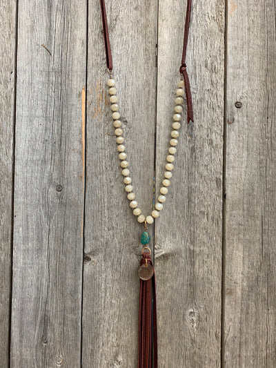 J.Forks Designs necklace hanging on wooden backdrop. This is a 30" Austrian opal crystal, bronze, and wine leather back necklace with an Indian Head Penny, Kingman Turquoise, and leather tassel.