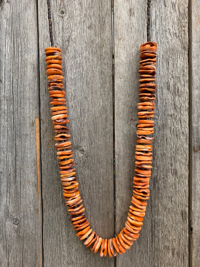 J.Forks Designs necklace on wooden backdrop. This is a 28" orange spiny oyster necklace with turquoise seeds, shell back, and solid bronze lobster claw clasp.