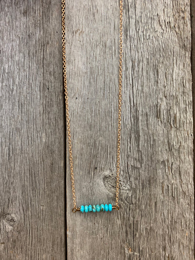 J.Forks Designs necklace hanging on a wooden backdrop. The necklace is 16" bronze chain with Kingman Turquoise center and bronze lobster claw clasp.