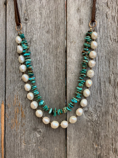 J.Forks Designs necklace on wooden backdrop. This is a two-strand 19" chip Kingman Turquoise, white freshwater pearls, bronze, and chocolate leather back necklace with Bronze Lobster Claw Clasp.