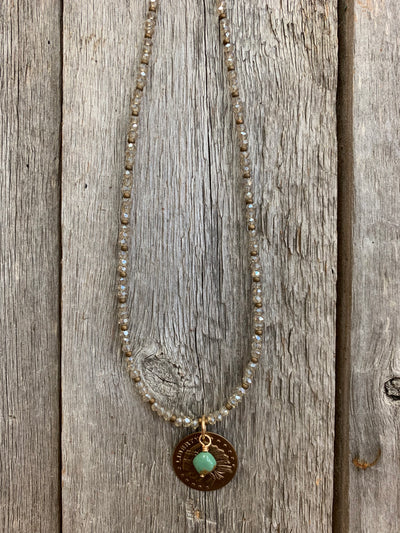 J.Forks Designs necklace on wooden backdrop. This is a 15" small Austrian crystal necklace with Kingman Turquoise and bronze Indian coin pendant with bronze lobster claw clasp.