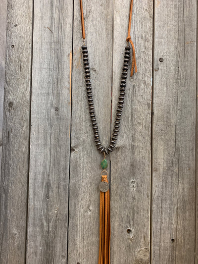 J.Forks Designs necklace hanging on wooden backdrop. This is a 32" Hand Carved Wood with Silver Inlay Bead necklace with Kingman Turquoise, buffalo nickel, cognac leather tassel, and cognac leather back.