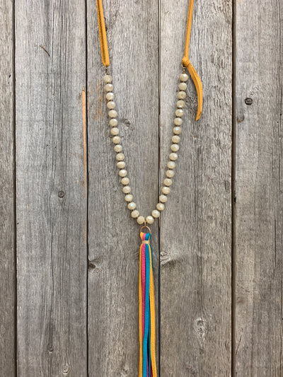 J.Forks Designs necklace hanging on wooden backdrop. This is a 30" Opal Austrian Crystal necklace with mustard, pink, and turquoise multi-color leather tassel and mustard leather back.