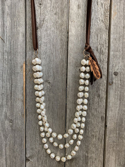 This is an image of the J.Forks Designs 3-Strand Freshwater Pearl with Side Feather Necklace hanging on a vintage wood backdrop. This image was taken in the J.Forks Designs studio located in Boerne, Texas. Just outside of San Antonio.