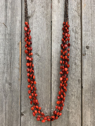 This is an image of the J.Forks Designs 5 Strand 36" Red Coral and Brown Pin Shell Necklace hanging on a on a vintage wood background. This photograph was taken at the J.Forks Designs studio on Main Street in Boerne, Texas. 