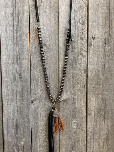 This is an image of the J.Forks Designs Hand-Carved Wood with Silver Inlay Beads and Double Feather and Tassel Necklace in Black hanging on a vintage wood backdrop. This image was taken in the J.Forks Designs studio located in Boerne, Texas. Just outside of San Antonio.