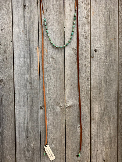 J.Forks Designs necklace hanging on wooden backdrop. This is a 70" saddle tan leather wrap necklace with Kingman Turquoise.