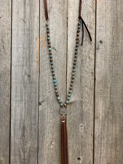 J.Forks Designs necklace hanging on wooden backdrop. This necklace is 32" gem silica and chocolate leather back with buffalo nickel and leather tassel drop.